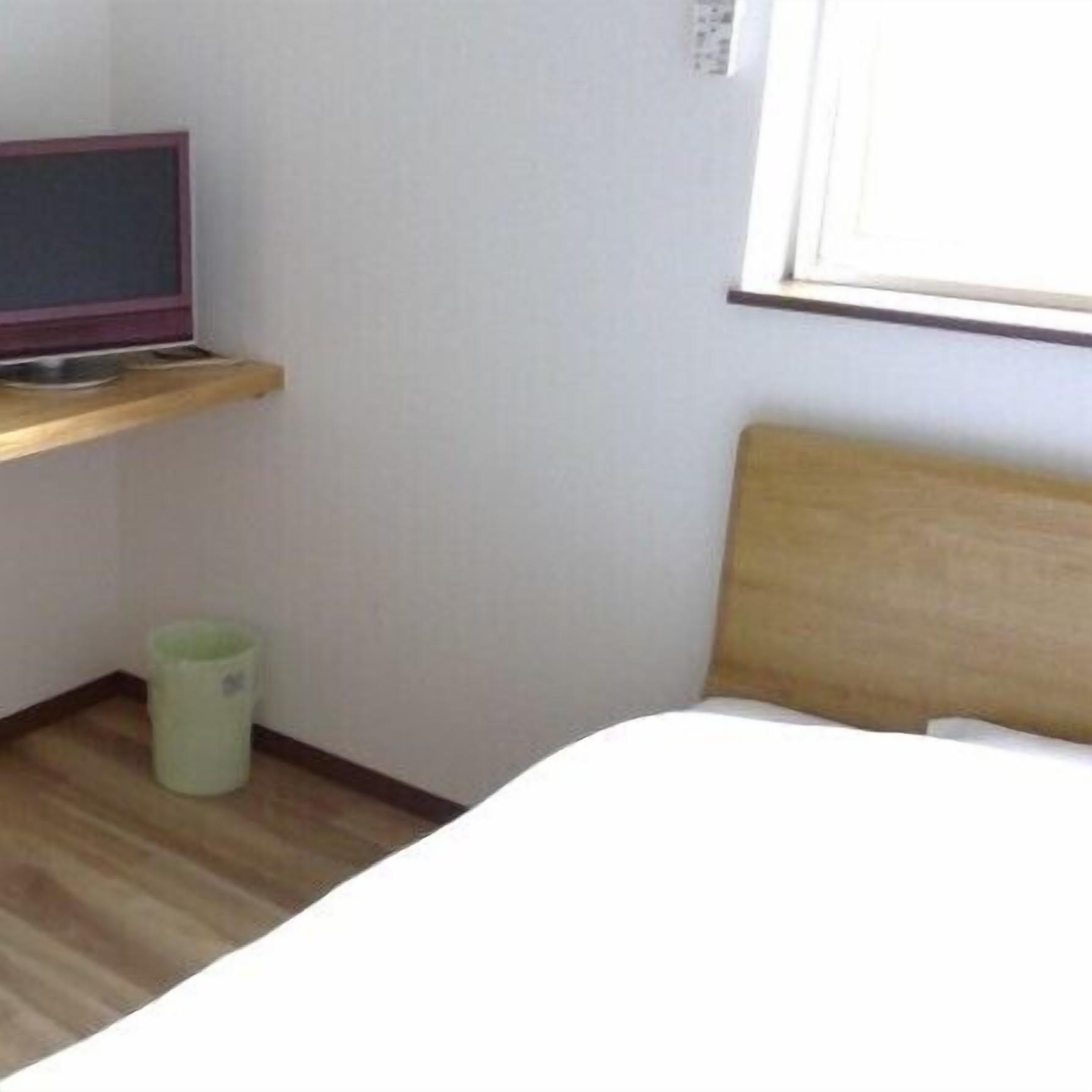 Een hotelkamer met een bed, een televisie op een plank en een prullenbak.