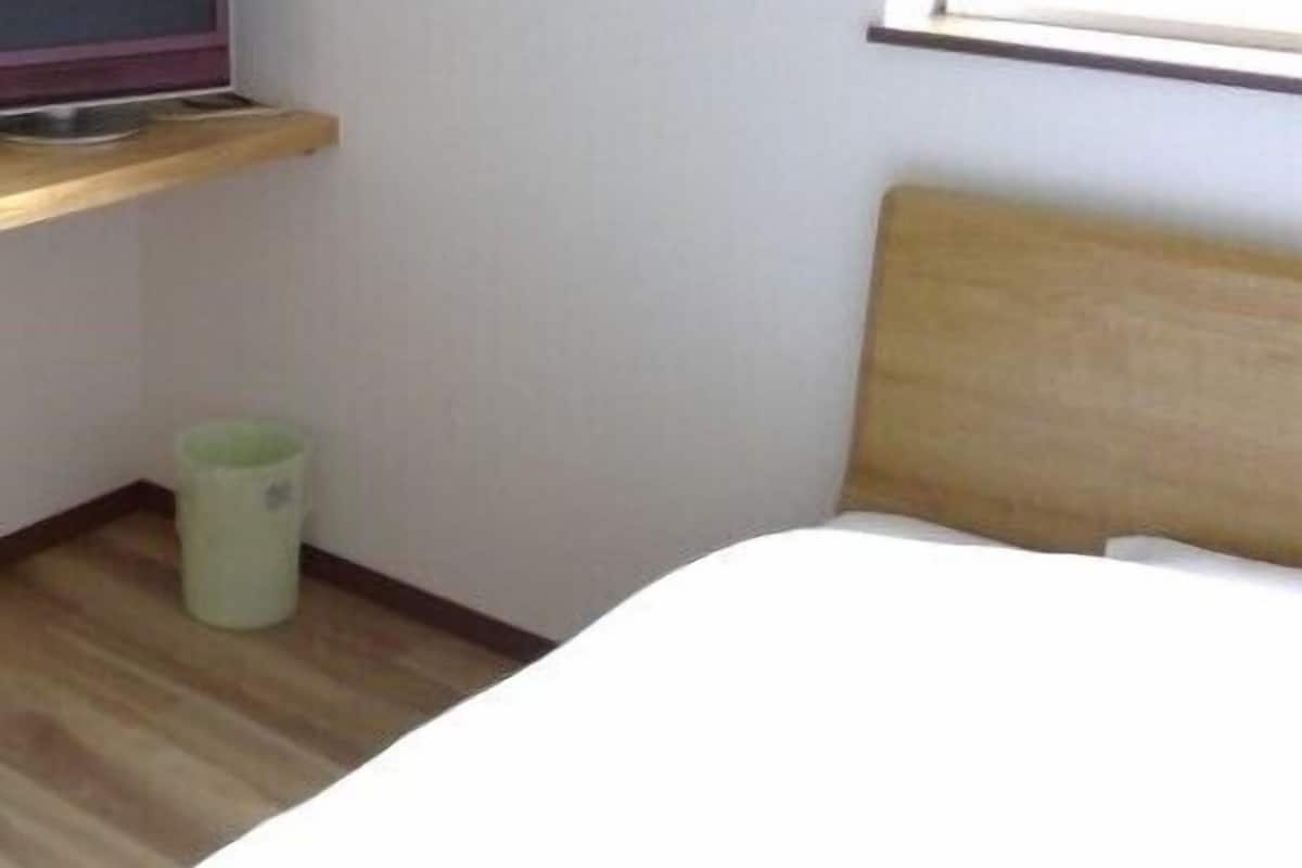 A hotel room with a bed, a television on a shelf, and a trash bin.