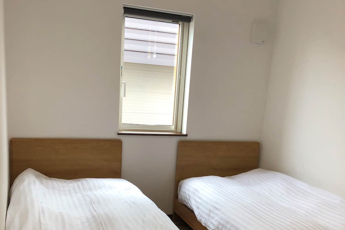 A bedroom with two wooden beds, a window with blinds, and a white wall.