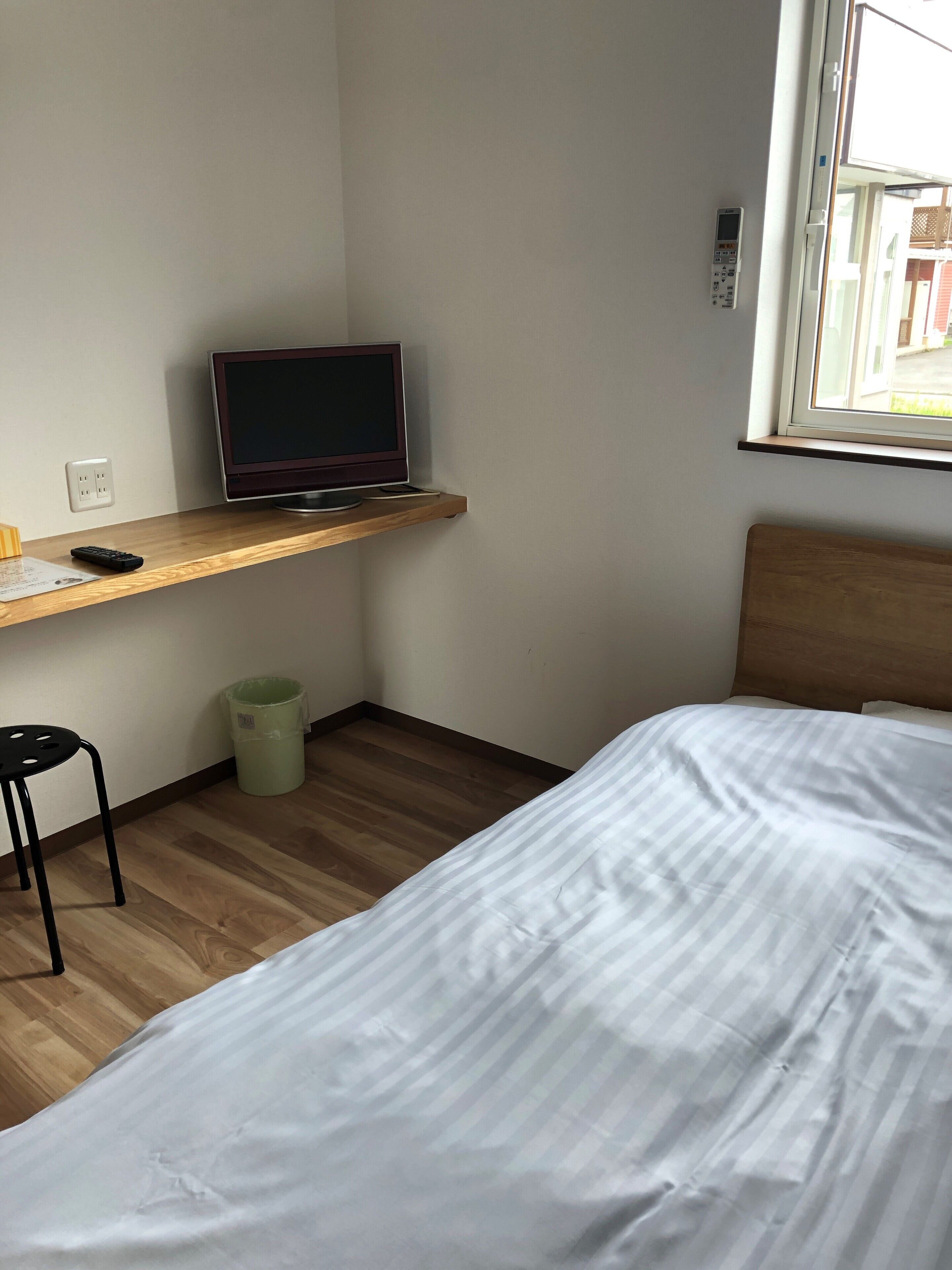 Quarto com cama, escrivaninha com computador, cadeira e janela.