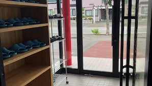 Schoenpresentatie met een houten plank en een metalen rek, een rode pilaar, en uitzicht op de straat buiten door een glazen deur.
