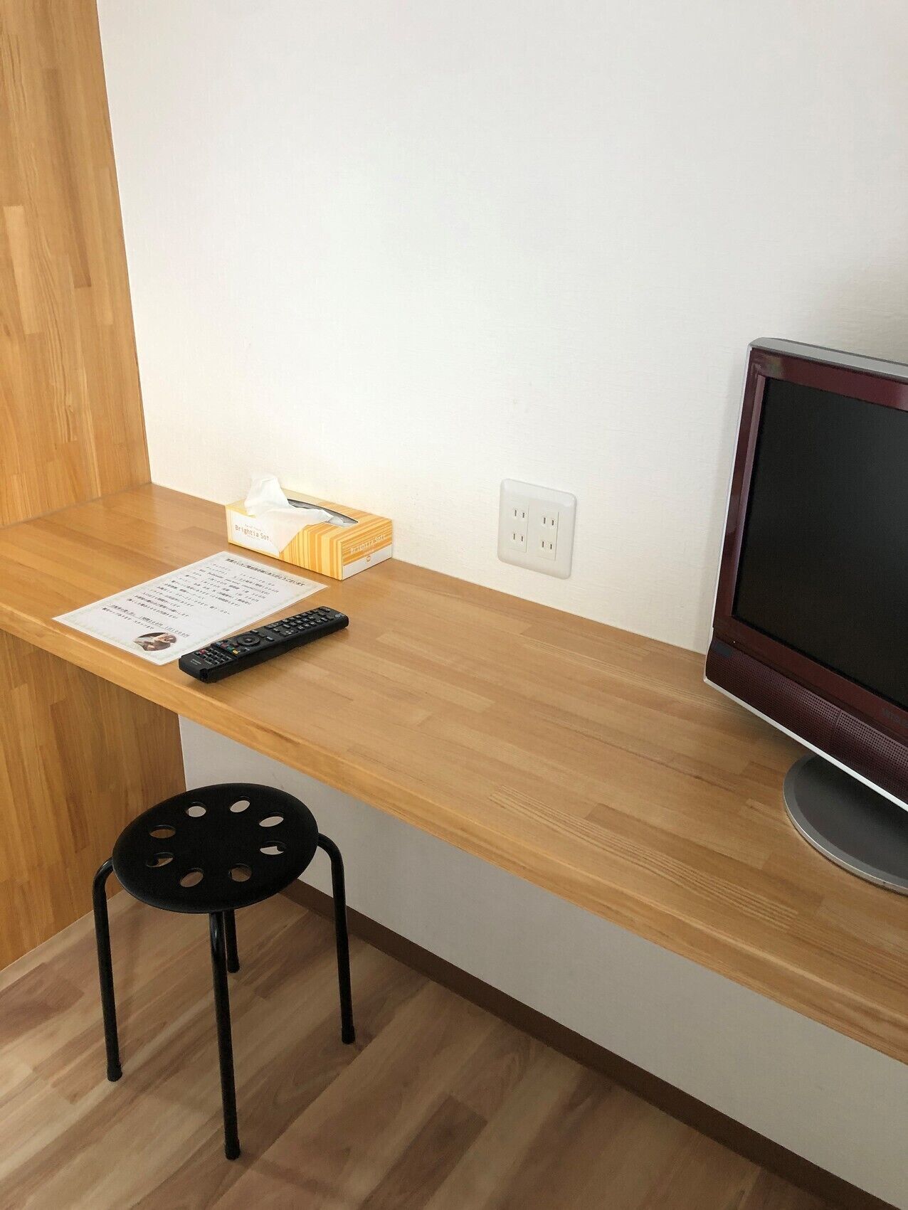 Een houten bureau met een afstandsbediening, een zakdoekendoos en een monitor.