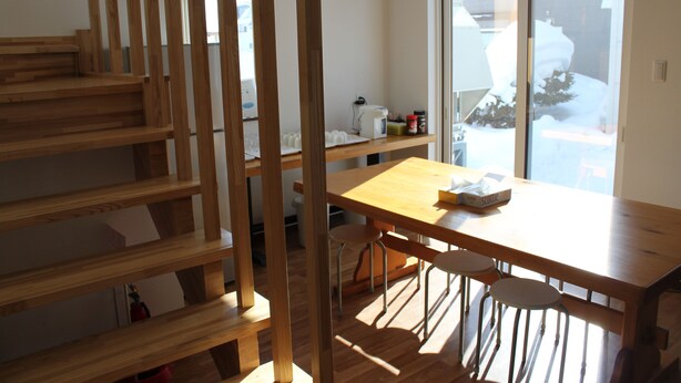 Een houten trap die leidt naar een eetgedeelte met een tafel en stoelen.