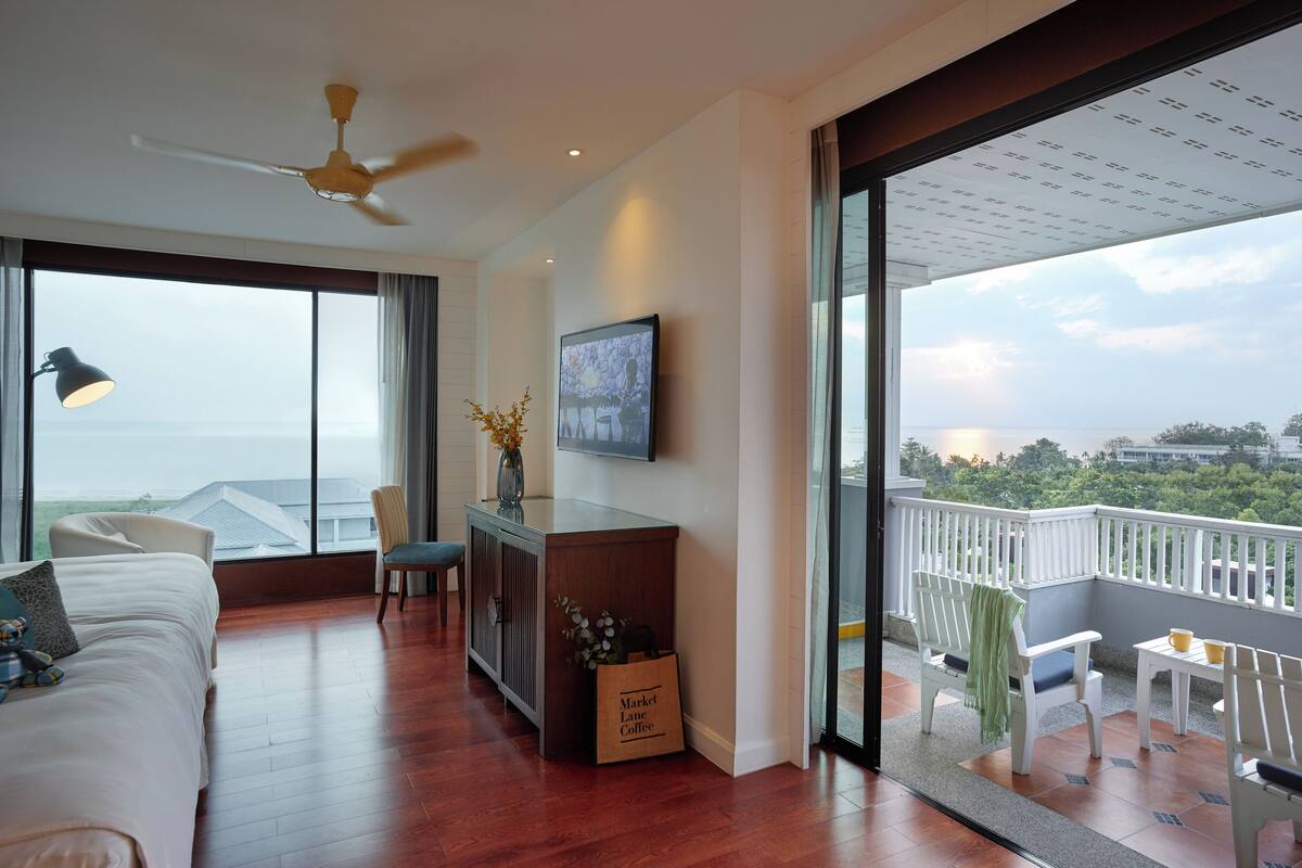 A spacious room with a large bed, a desk, and a balcony with a view of the city.