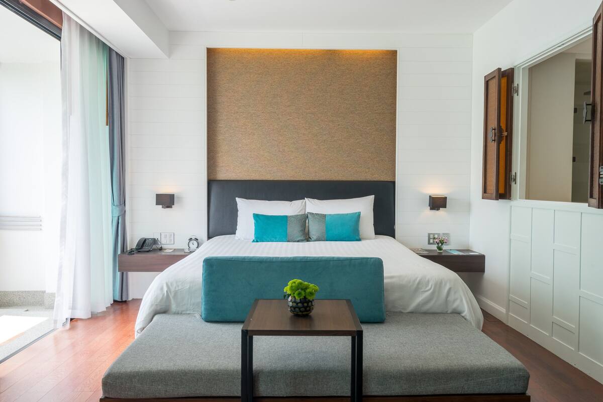 A hotel room with a large bed, a bedside table, a small table with a plant, and a large mirror.