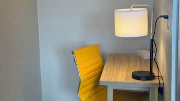 Een hoekzaal met een gele stoel, een houten tafel, een bureaulamp en een prullenbak.