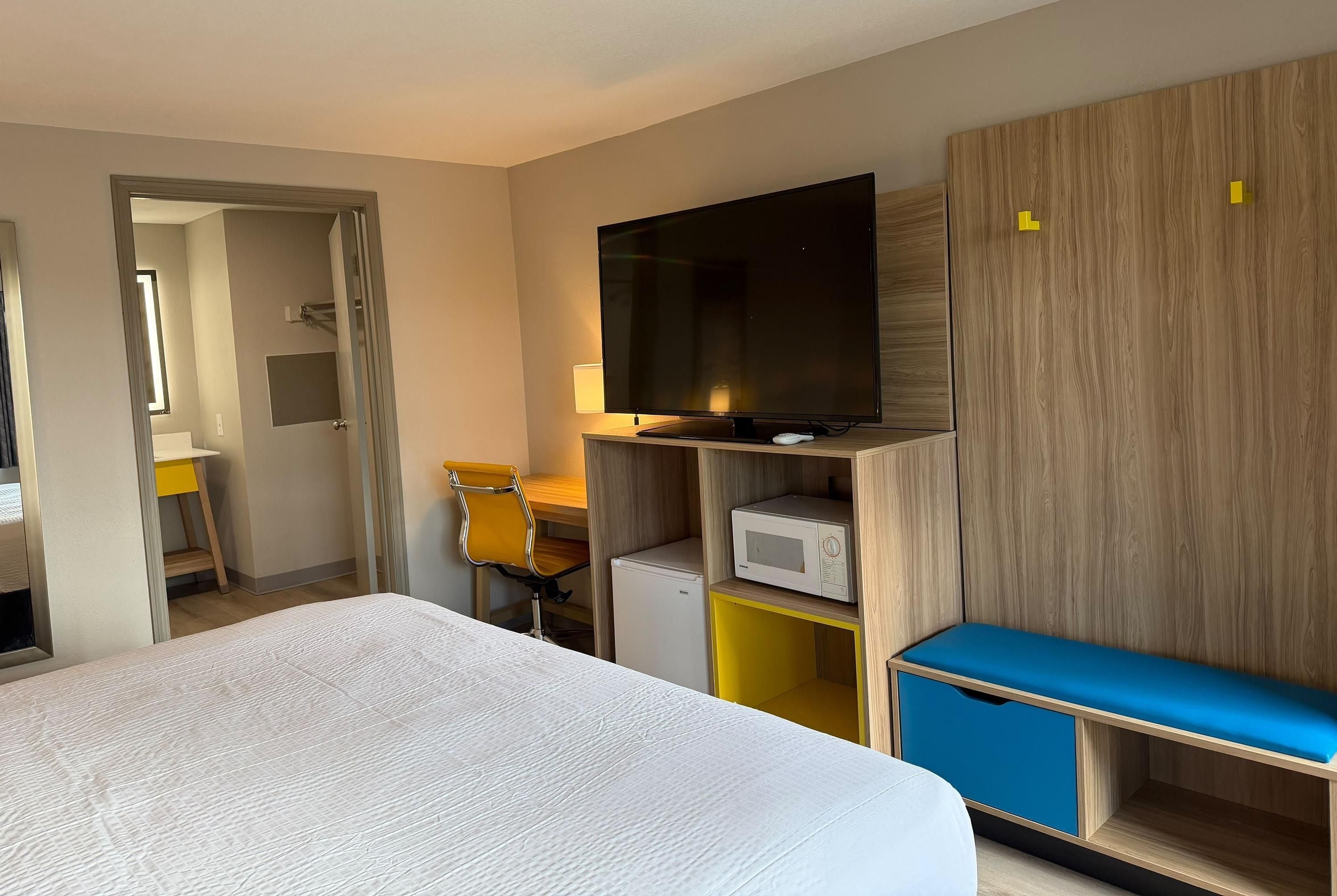 Hotellihuone, jossa on sänky, televisio, mikroaaltouuni, työpöytä ja tuoli.