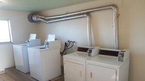 A laundry area with two washing machines and two dryers, connected by a metal duct system. - Split Mountain Motel (Vernal)