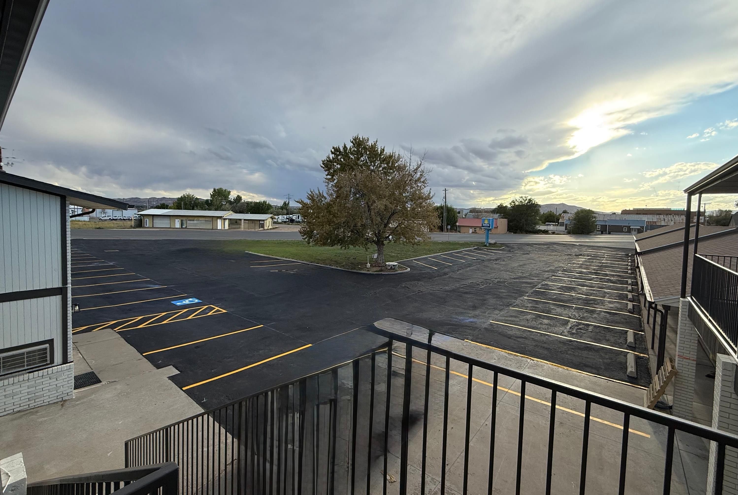 A parking lot with marked spaces, a building with a flat roof, and a tree in the center.