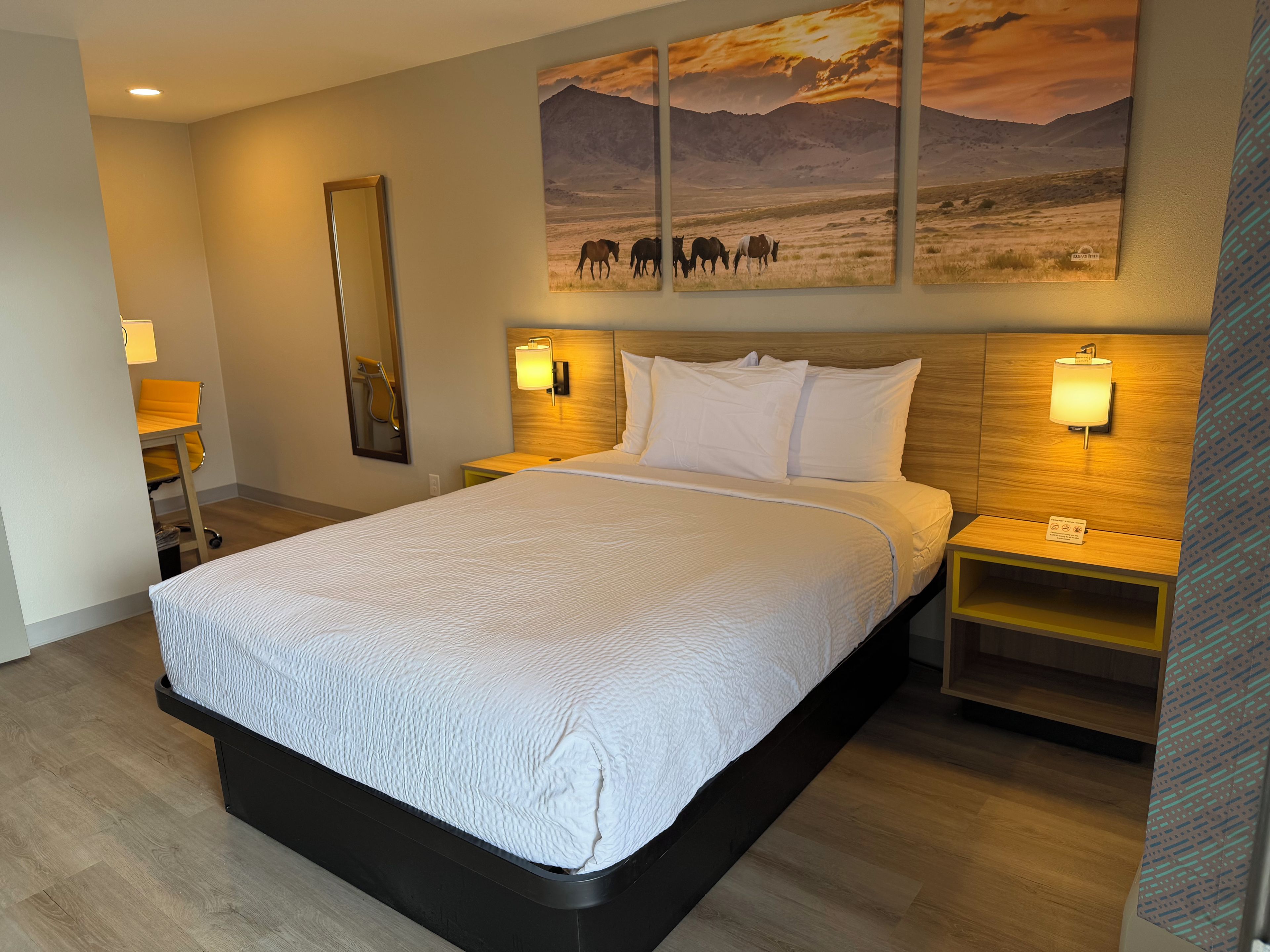 A hotel room with a large bed, two bedside tables, a mounted painting, and a mirror.