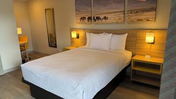 A hotel room with a large bed, two bedside tables, a mounted painting, and a mirror.
