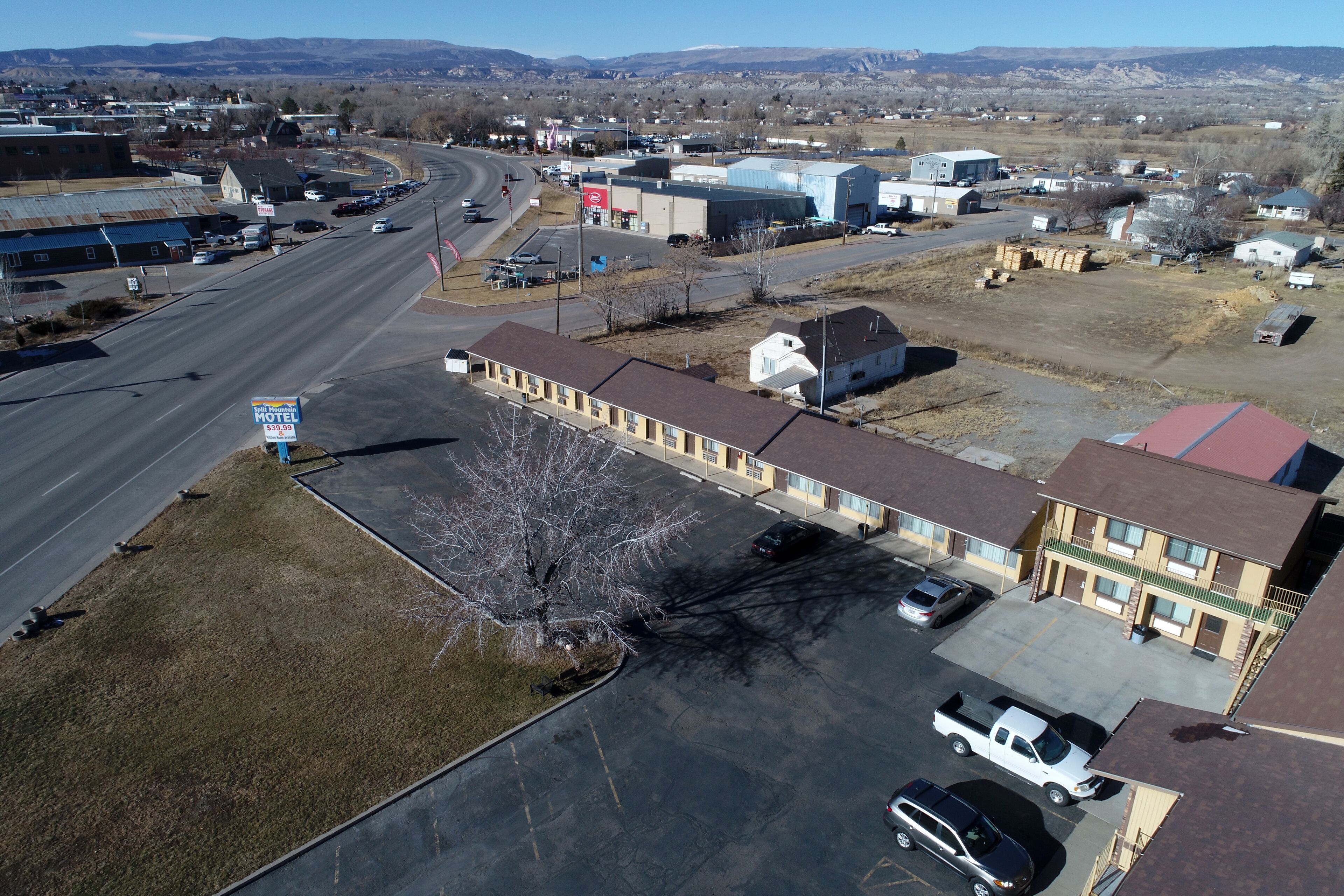 A motel with a parking lot, a building with a red roof, and a road in the background.
