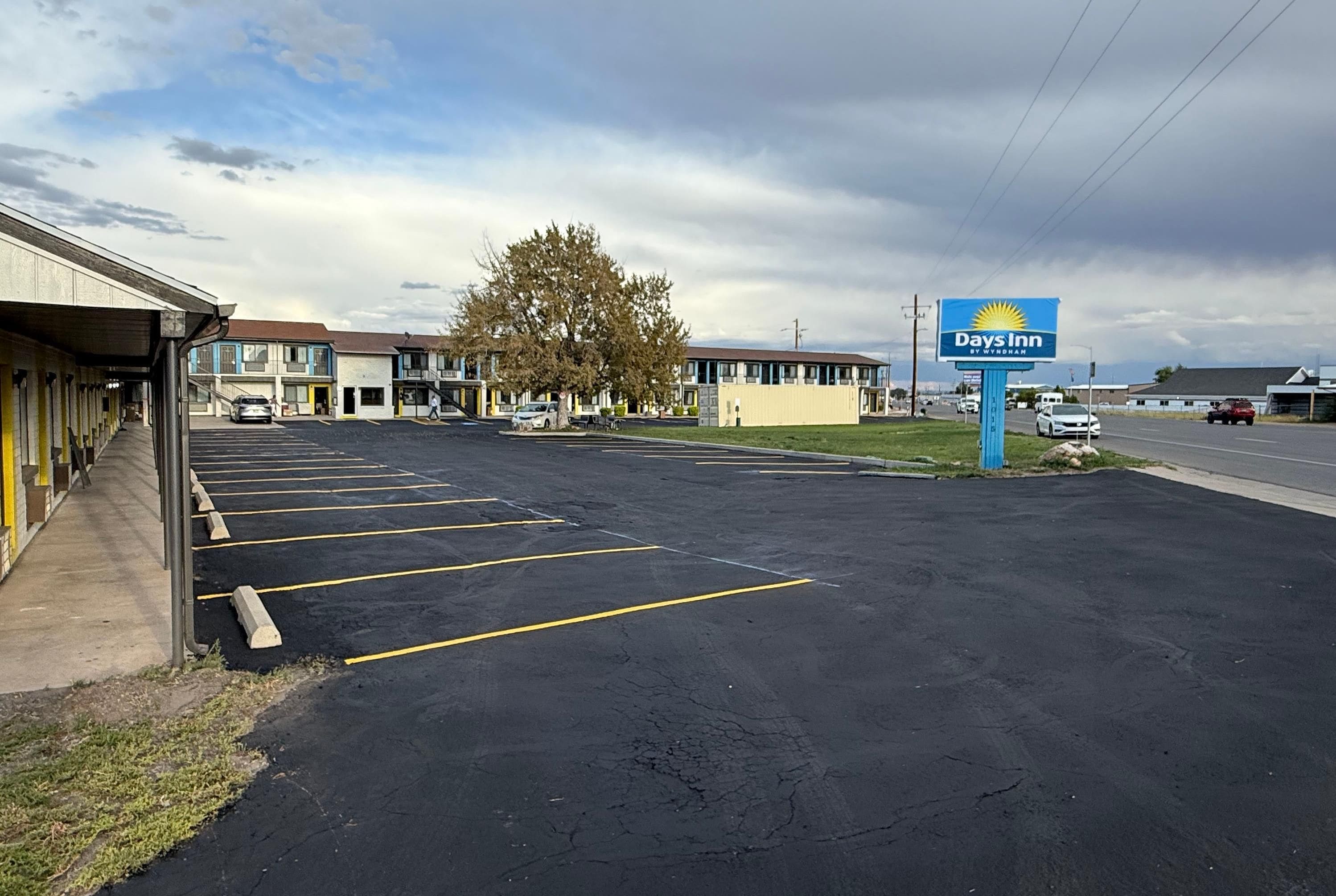 Un motel Days Inn avec un parking, un grand arbre et une route en arrière-plan.
