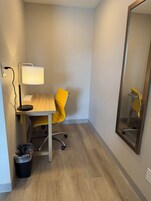 Habitación de hotel con escritorio, silla, lámpara y un espejo grande.