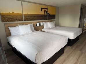 Une chambre d’hôtel avec deux lits, une grande peinture représentant un champ pétrolier et une tête de lit en bois.