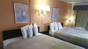 A hotel room with two beds, each with white linens and multiple pillows. There are wall-mounted lamps and framed floral artwork above the beds. - Split Mountain Motel (Vernal)