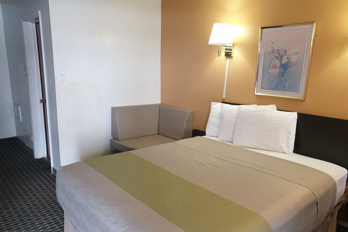 A hotel room with a bed, a nightstand, a chair, a lamp, and a painting on the wall.