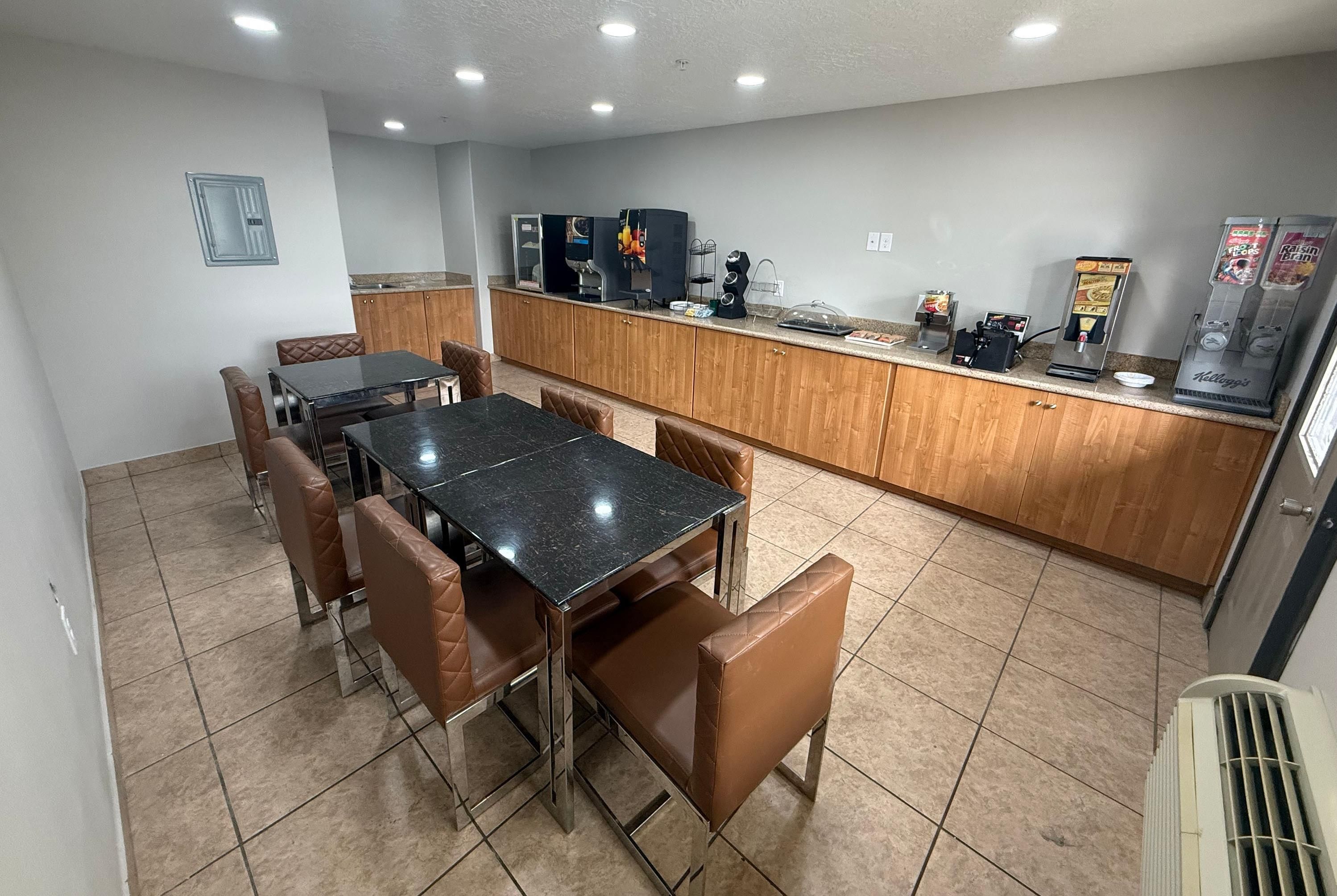 Un coin repas avec une table en marbre noir et des chaises en cuir marron, une cuisine avec des meubles en bois et un distributeur de boissons.