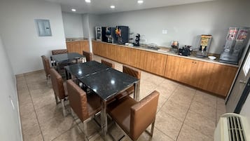 A dining area with a black marble table and brown leather chairs, a kitchen with wooden cabinets, and a beverage dispenser.