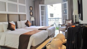A hotel room with two beds, a balcony, a chair, a table with a lamp, and a TV.