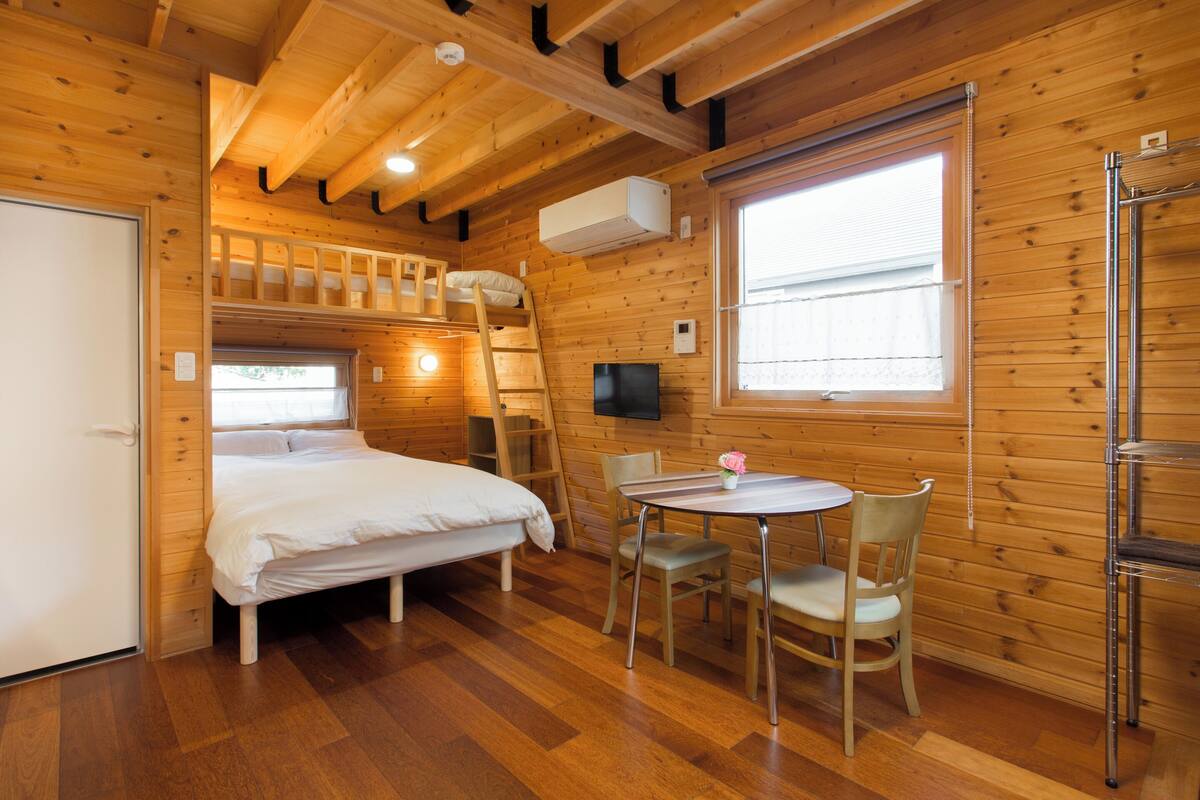 A wooden cabin with a bunk bed, a dining area with a table and chairs, and a TV mounted on the wall.