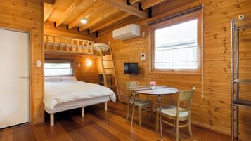Uma cabana de madeira com uma cama de beliche, sala de jantar com mesa e cadeiras, e uma TV fixada na parede.