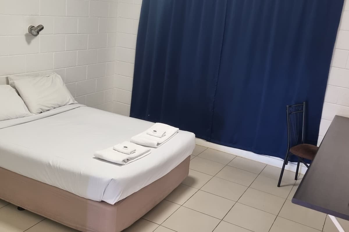 A neatly arranged bedroom with a bed, a wooden dresser, a desk with a chair, and a blue curtain.