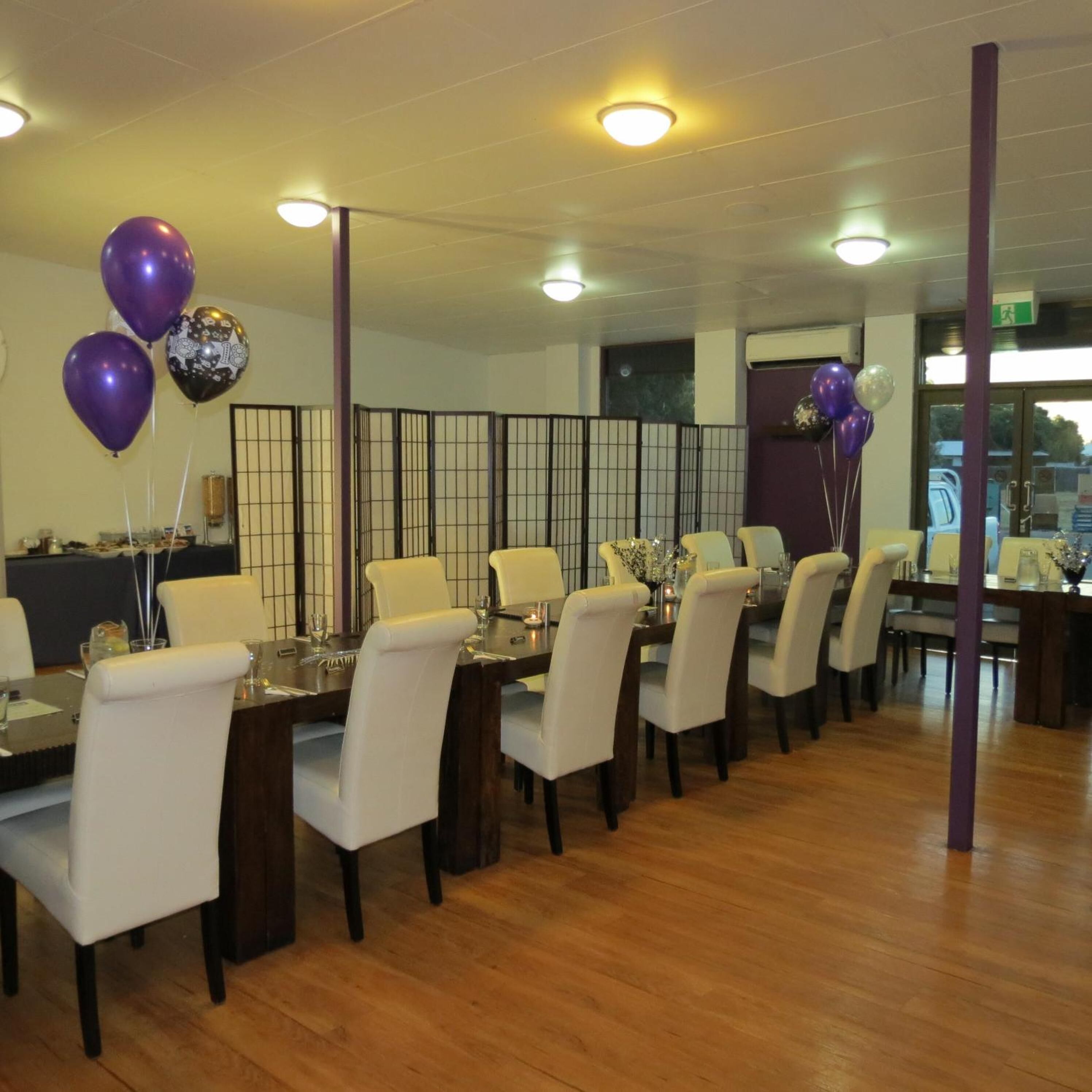 Un restaurante con varias mesas, sillas blancas y globos morados.
