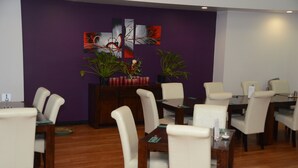 A dining area with a purple wall, a wooden buffet, and white chairs. - Capricorn Hotel (Blackwater)