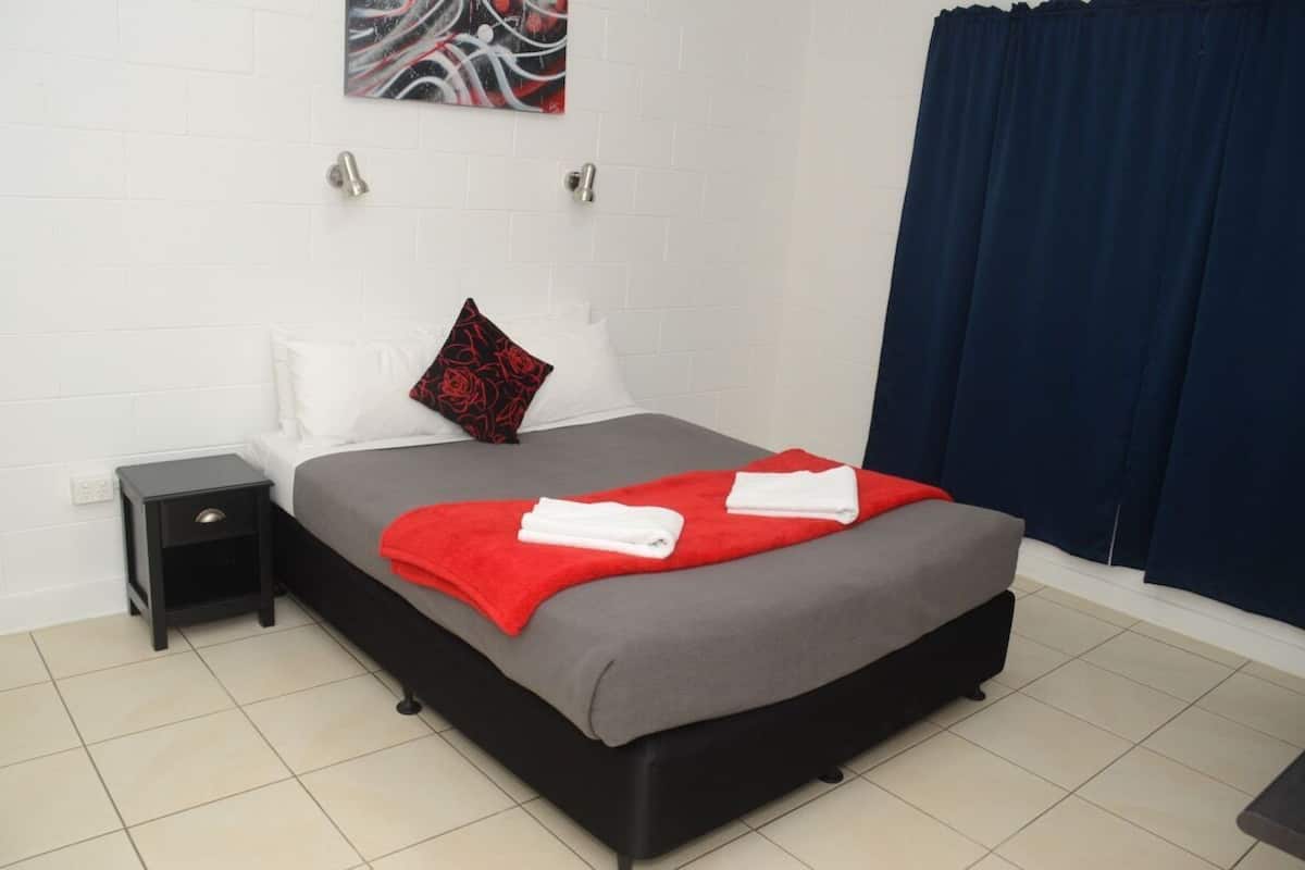 A neatly made bed with a grey and red blanket, a black nightstand, a white pillow, and a red pillow with a floral design.