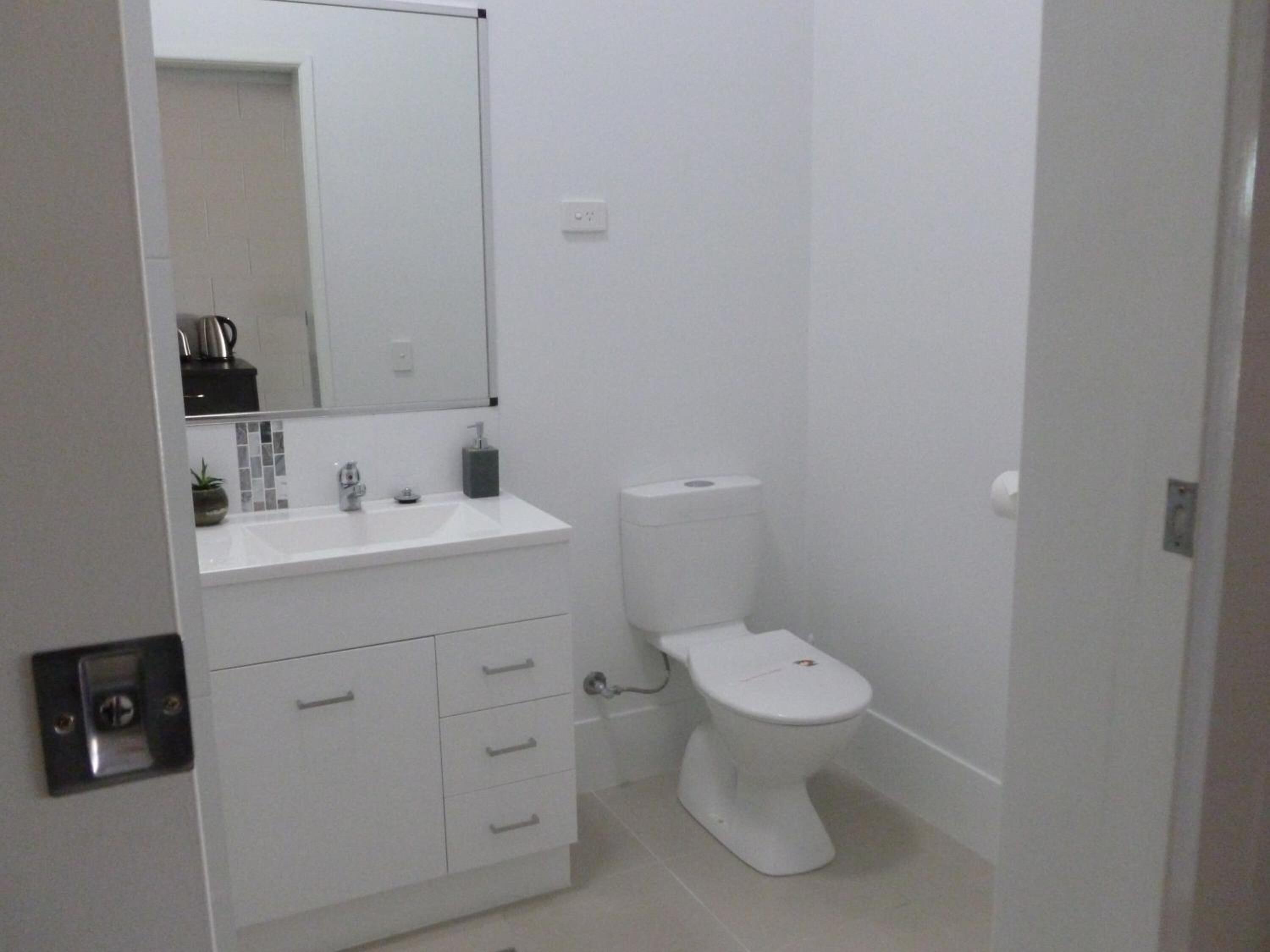 A modern bathroom with a white sink, mirror, and toilet.