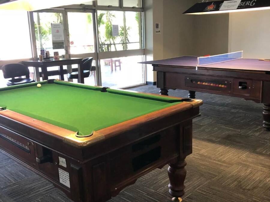 Ein Billardtisch mit grüner Spielbahn, ein Billardqueue und ein Spielball. Über dem Tisch hängt eine Leuchte.