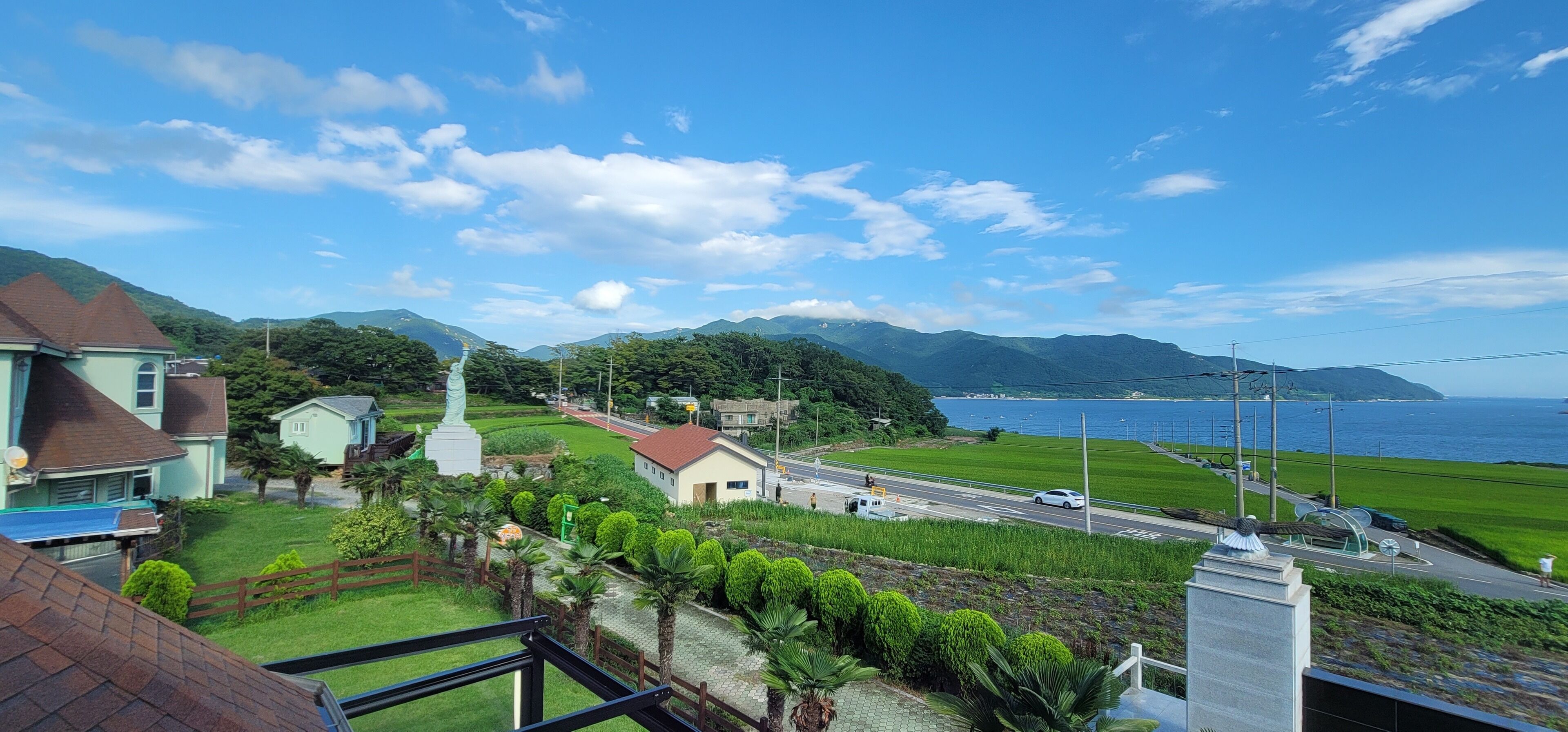 A coastal town with a statue, houses, and a road leading to the sea.