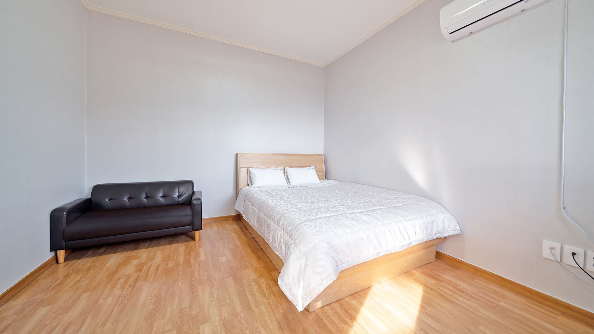 Ein Schlafzimmer mit einem Bett, einer schwarzen Ledersofa, Holzboden und einer Klimaanlage.