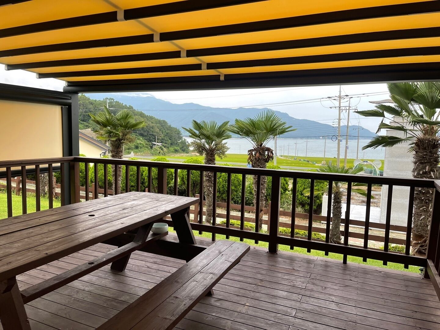 A wooden deck with a picnic table and a railing, overlooking a scenic view of mountains and a body of water.