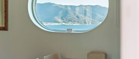 A room with a round window overlooking a coastal landscape, a table with chairs, and a small sign on the window.