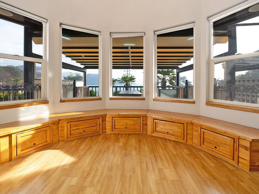 Habitación de esquina con ventanas amplias, muebles de madera y vistas al exterior.
