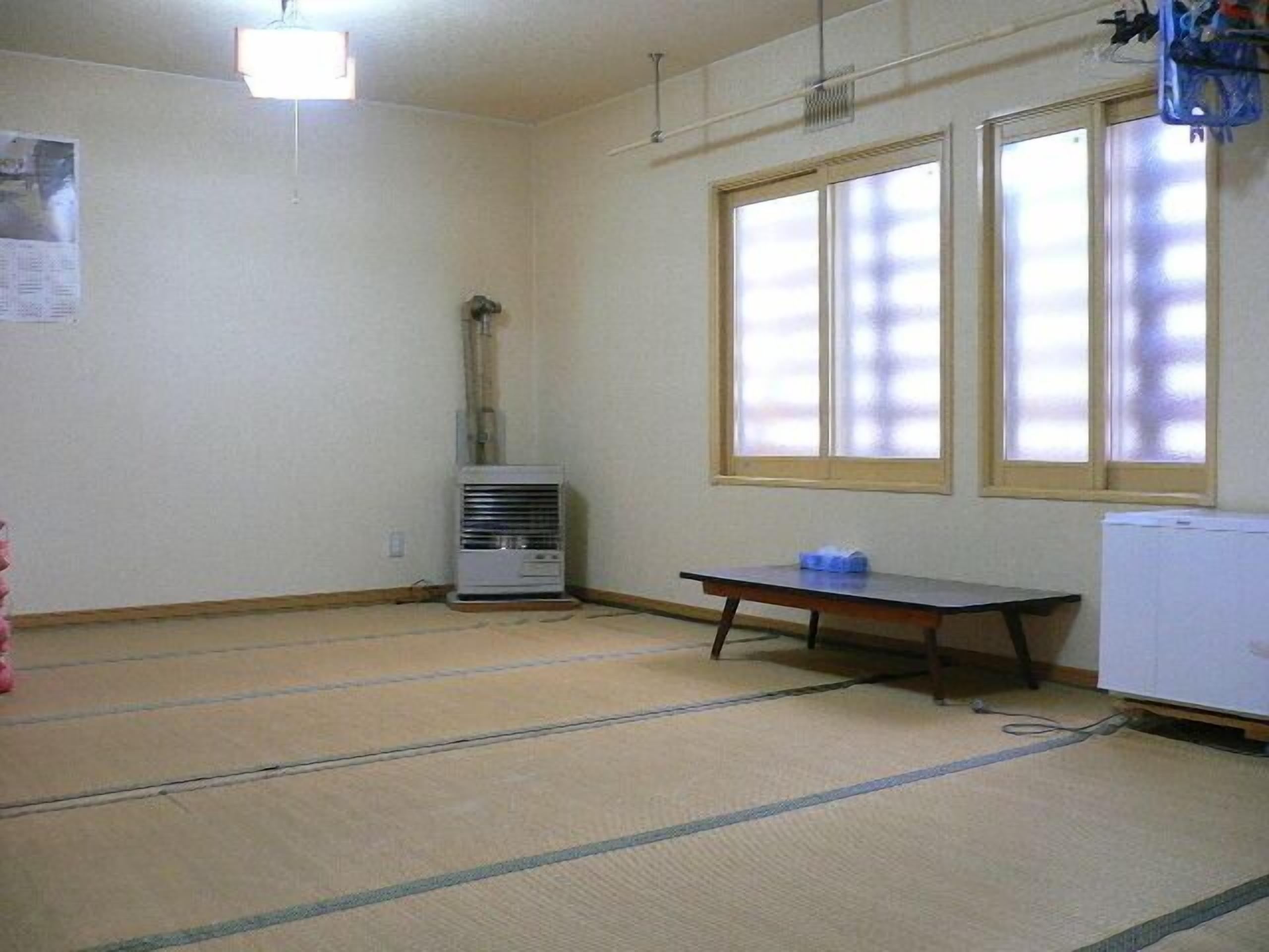 Ein Zimmer mit Tatami-Böden, einem Heizkörper, einem Tisch und einem Fenster.