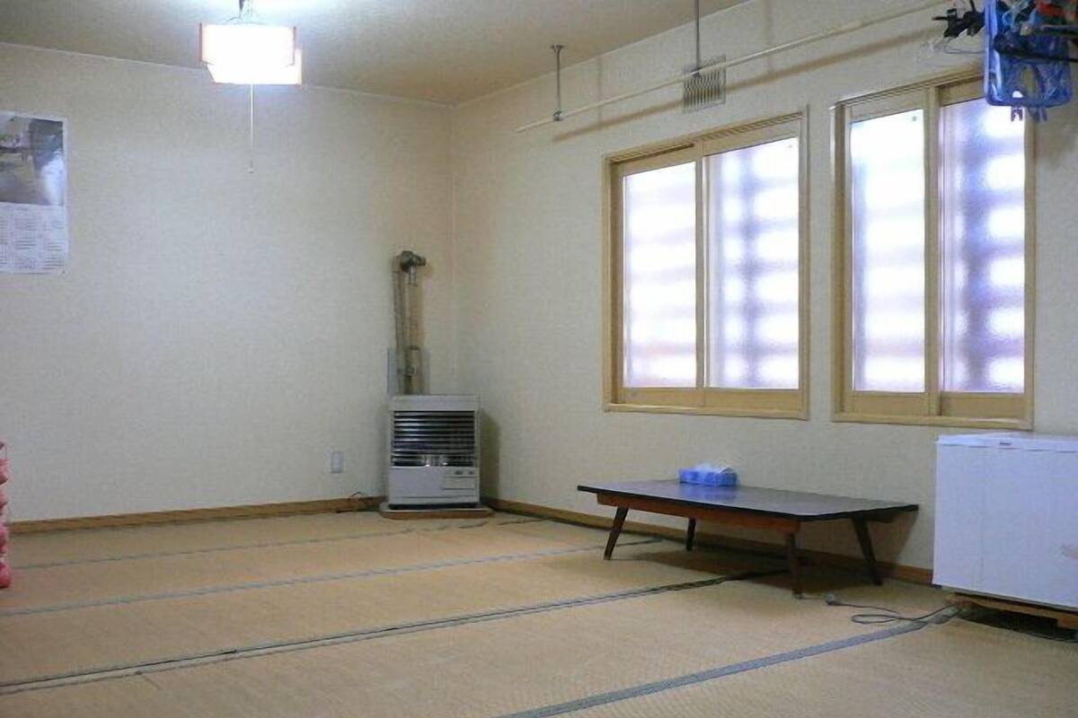 Una habitación con suelo de tatami, un calentador, una mesa y un ventanal.