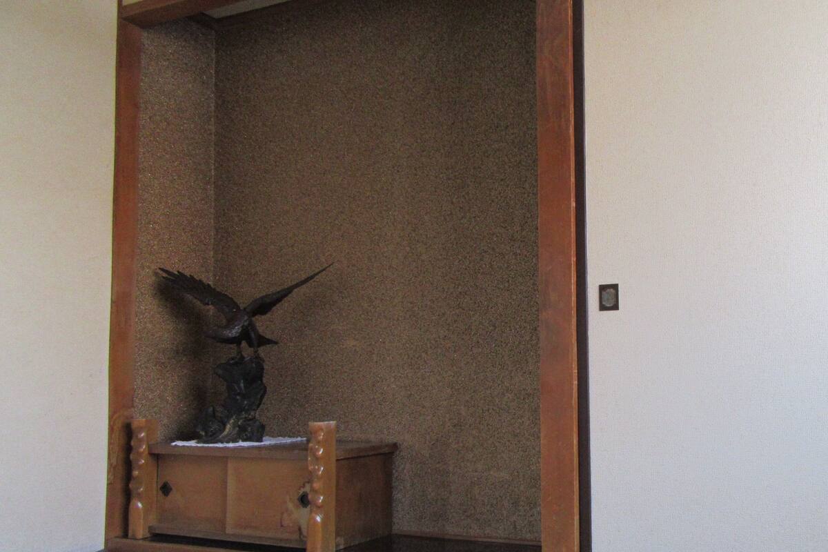 Una habitación con suelo de tatami, un armario de madera con una estatua y una puerta corredera.