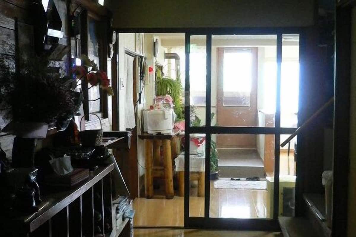 A narrow hallway with a wooden floor leading to a room with a sliding glass door.