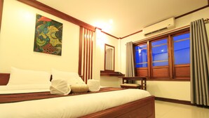 A hotel room with a wooden bed, a painting on the wall, a desk, and a window with curtains. - Lao Silk Hotel (Vientiane)