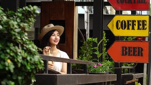 A person sitting at a table with a drink, with signs for coffee and beer in the background. - Lao Silk Hotel (Vientiane)