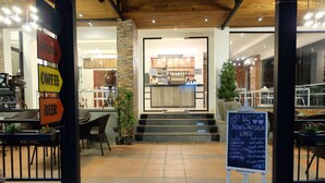 A cafe entrance with a signboard listing coffee and beer options, a chalkboard menu, and a staircase leading to the cafe area. - Lao Silk Hotel (Vientiane)