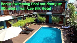A swimming pool with lounge chairs and umbrellas, located outside a hotel with a wooden deck and a balcony. - Lao Silk Hotel (Vientiane)