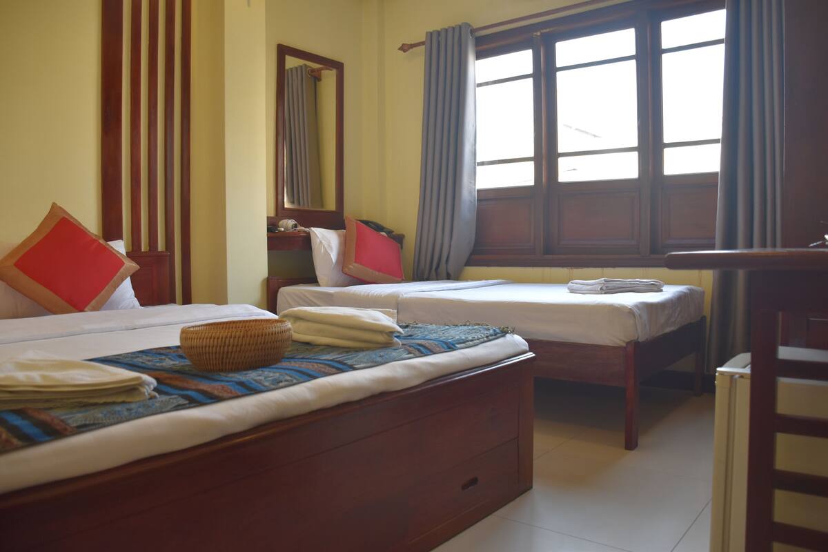 A room with two beds, a wooden dresser, a mirror, and a window with curtains.