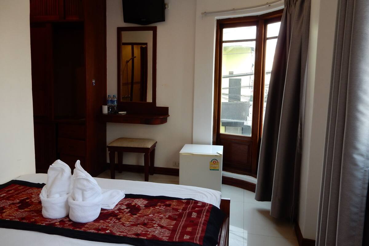 A hotel room with a bed, a desk, a chair, a television, and a window with curtains.