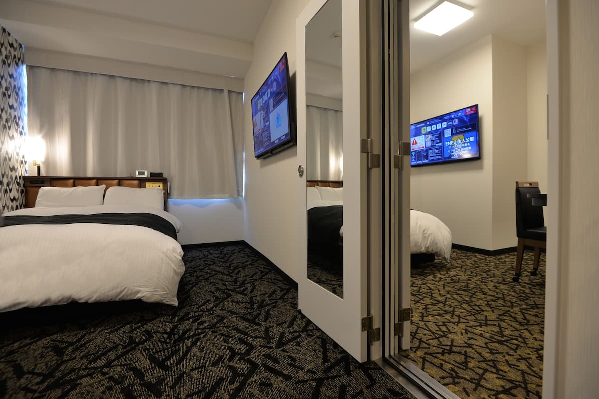 A hotel room with a large bed, a desk with a computer, and a television mounted on the wall.