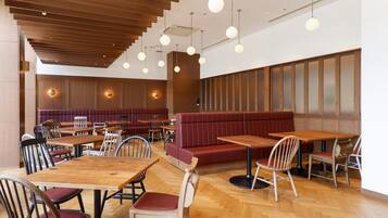 A restaurant with wooden tables and chairs, a red booth, and pendant lighting.