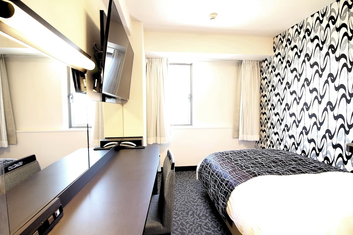 A hotel room with a bed, a desk, a flat-screen TV, and a patterned wall.